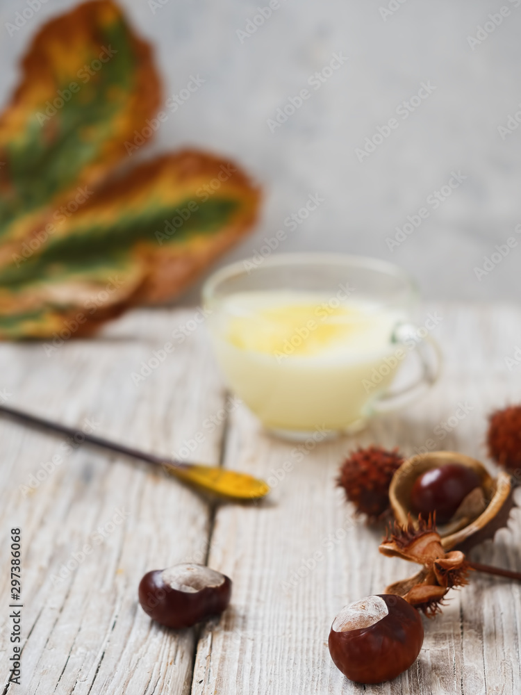 Chestnuts on a wooden surface. In the background is a glass cup with golden milk and a leaf of chestnut. Close-up. Chestnuts on a wooden surface. In the background is a glass cup with golden milk and a leaf of chestnut. Close-up.