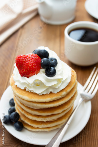 Pancakes with cream, berry and coffee cup over rustic wooden background, copy space for text.