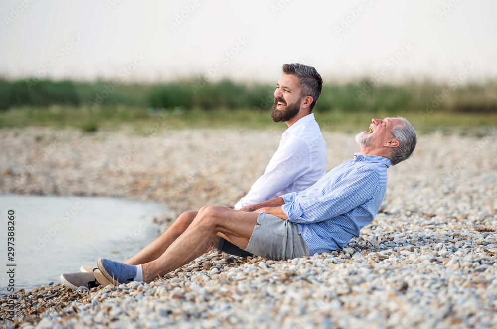 Senior father and mature son sitting by the lake. Copy space.
