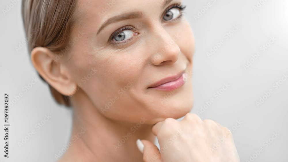 Beautiful female face with first wrinkles smiling looking at camera isolated at light background Beautiful female face with first wrinkles smiling looking at camera isolated at light background