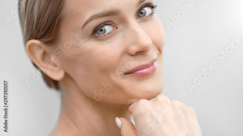 Beautiful female face with first wrinkles smiling looking at camera isolated at light background photo