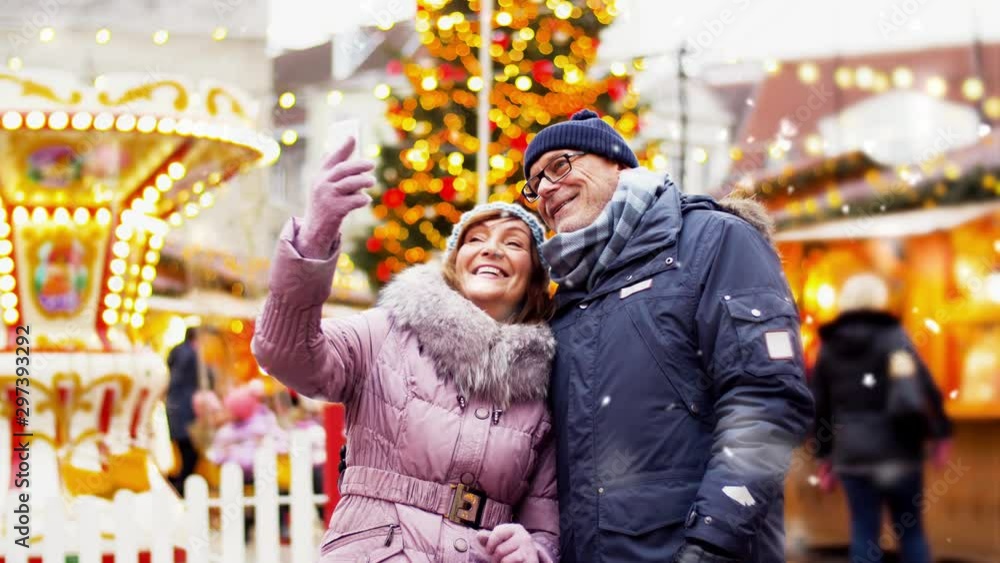 technology, winter holidays and people concept - happy senior couple taking selfie by smartphone at christmas market on town hall square in tallinn, estonia technology, winter holidays and people concept - happy senior couple taking selfie by smartphone at christmas market on town hall square in tallinn, estonia