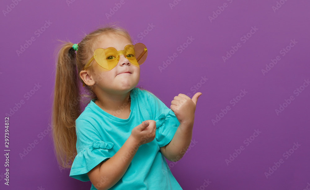 Portrait of little child girl heart shaped sunglasses isolated on purple background. Shows thumbs up, everything is ok. Happy childhood, wow and shock concept Portrait of little child girl heart shaped sunglasses isolated on purple background. Shows thumbs up, everything is ok. Happy childhood, wow and shock concept