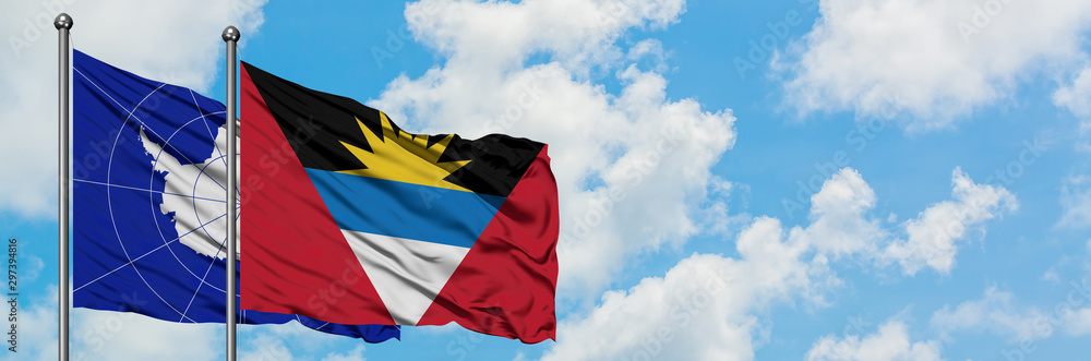 Antarctica and Antigua and Barbuda flag waving in the wind against white cloudy blue sky together. Diplomacy concept, international relations.