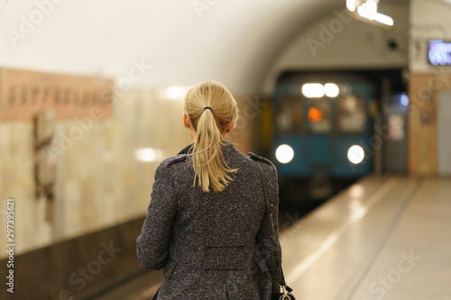 Photography of a woman waiting for the train car in Moscow subway. Image with train as defocused background.