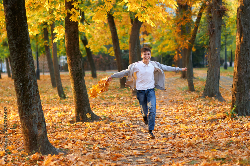 Boy teenager having holiday in autumn city park, running, smiling, playing and having fun. Bright yellow trees and leaves Boy teenager having holiday in autumn city park, running, smiling, playing and having fun. Bright yellow trees and leaves