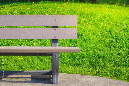 Empty brown bench on green grass and yellow flowers with bright sun light in the city park during summer sunny day