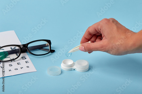 Flat composition with contact lenses, table for eye examination. Accessories for ophthalmologists. Glasses and lenses for vision correction on a blue background