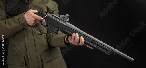 A man in a green jacket with a bolt carbine in his hands on a black background. A hunter or soldier with a weapon on hand. Modern sniper rifle. Weapon for firing at long distances.