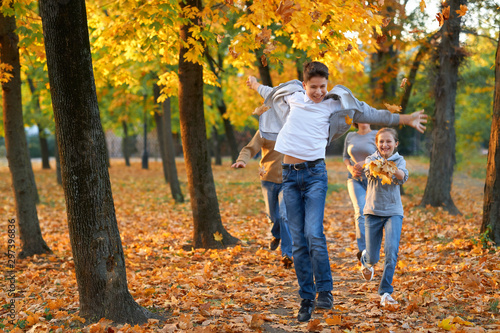 Happy family having holiday in autumn city park. Children and parents running, smiling, playing and having fun. Bright yellow trees and leaves