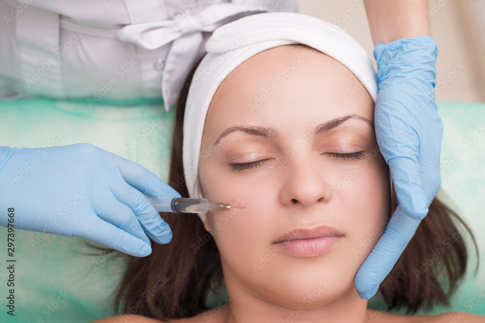 injection into the skin of the face of a young woman, close up. Doctor cosmetologist using a syringe with a needle, injects a remedy for facial wrinkles