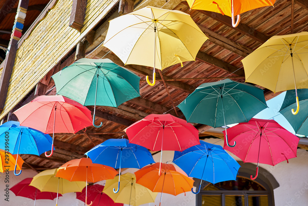 Colorful umbrellas hang on the street under a wooden bridge.
