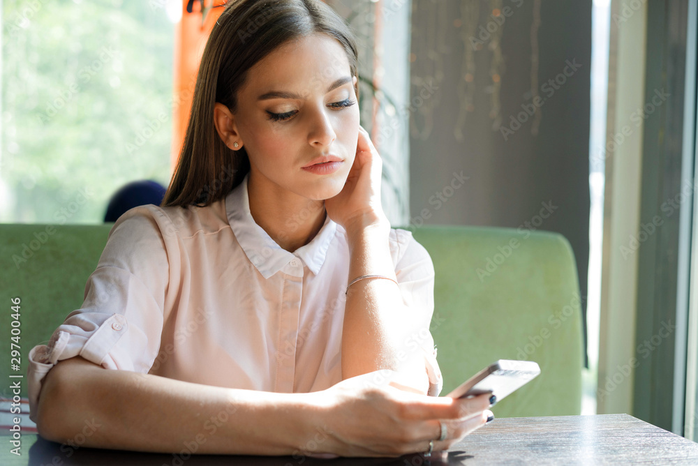 Girl reads messages on the phone while sitting in a cafe. Girl reads messages on the phone while sitting in a cafe.