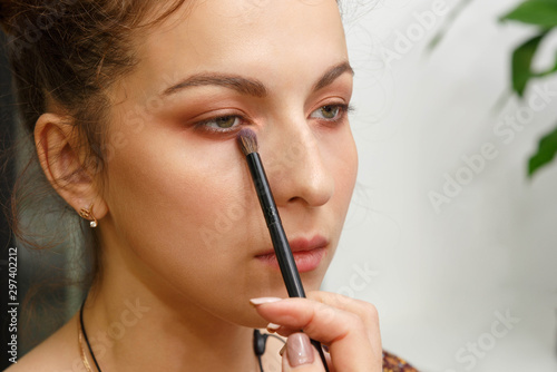 The process of creating makeup. Makeup artist working with a brush on the face of the model.