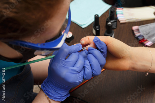 The master of nail service applies a transparent varnish to the clients nail.