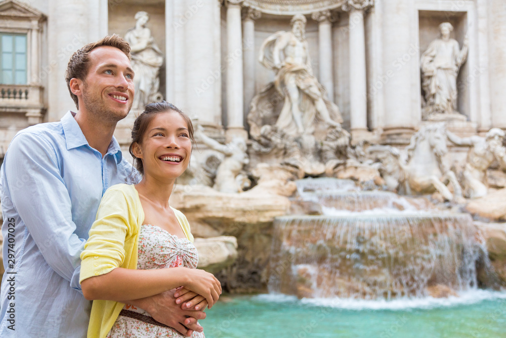 Rome travel tourists couple at Trevi Fountain in Rome, Italy vacation. Happy young romantic interracial couple traveling in Europe. Man and Asian woman embracing together. - obrazy, fototapety, plakaty 