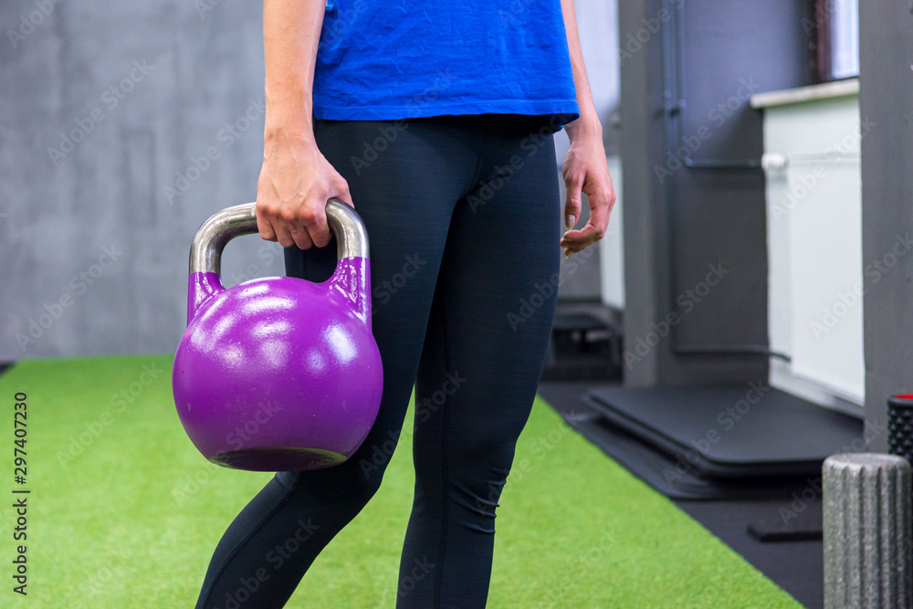 Naklejka premium Detail shor of female holding purple kettlebell in her hand.