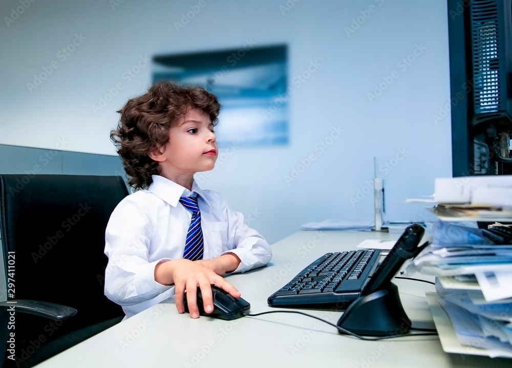 Cute beautiful little boy children play as office worker sitting on working desk using business computer and working hard in a modern office Cute beautiful little boy children play as office worker sitting on working desk using business computer and working hard in a modern office