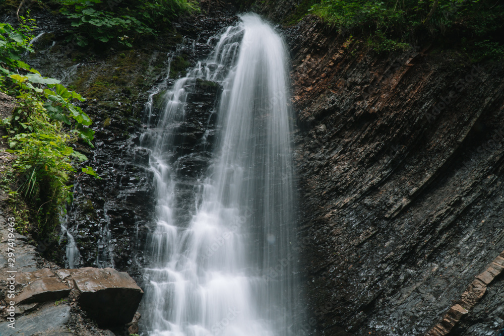 Fototapeta premium Beautiful waterfall in summer. A fast waterfall. View of the waterfall from below