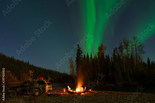 Northern Lights above people camping next to river with campfire