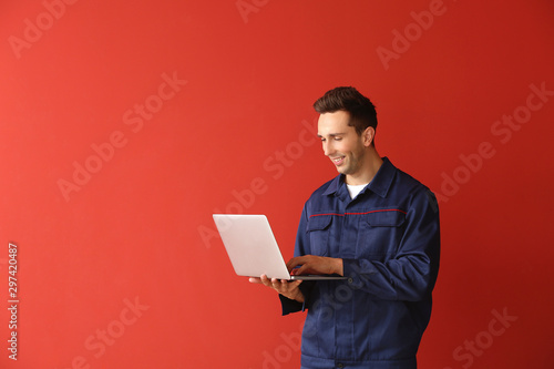 Male car mechanic with laptop on color background