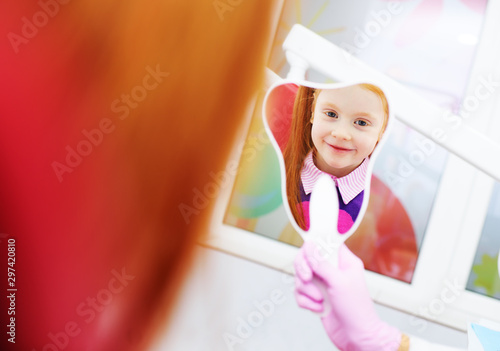 child-a little red-haired girl smiling looking in the mirror sitting in the dental chair.