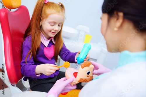 the baby is a little red-haired girl and a female pediatric dentist playing doctor with toy dental instruments sitting in the dental chair.