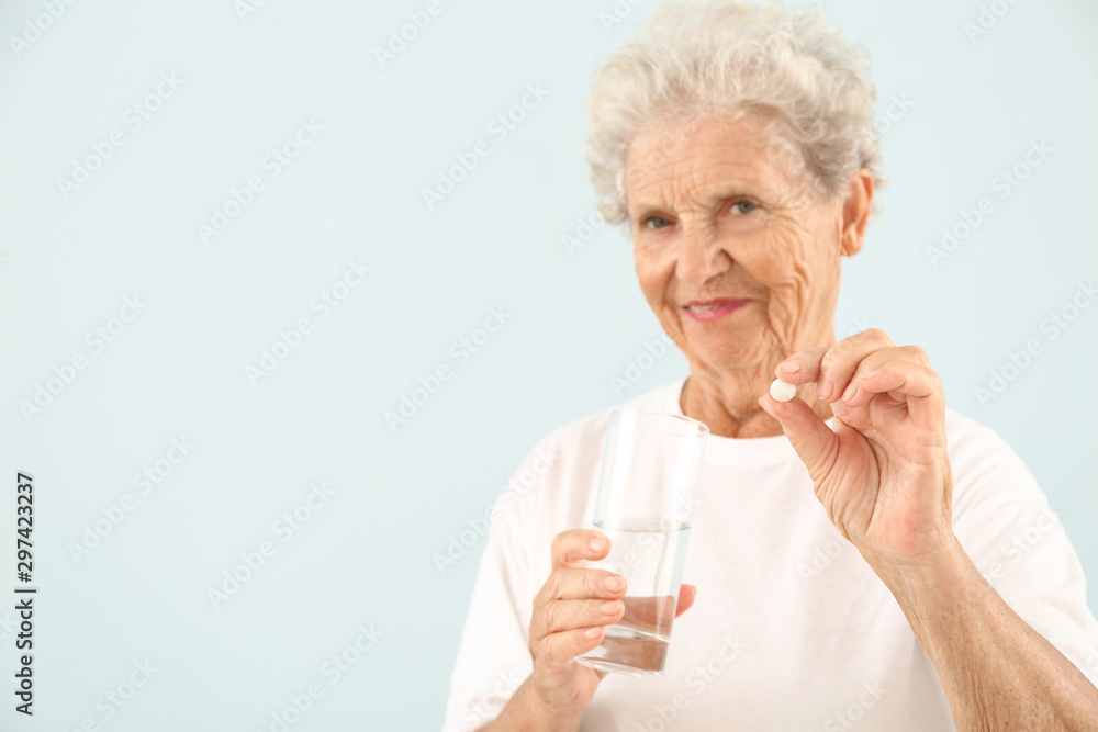 Elderly woman taking pill on light background Elderly woman taking pill on light background