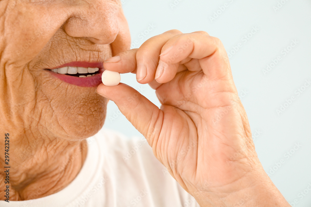 Elderly woman taking pill on light background, closeup Elderly woman taking pill on light background, closeup