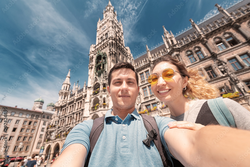 Fototapeta premium happy multinational couple in love hugs and takes a selfie photo on the background of The city hall tower in Munich. Honeymoon trip to Germany