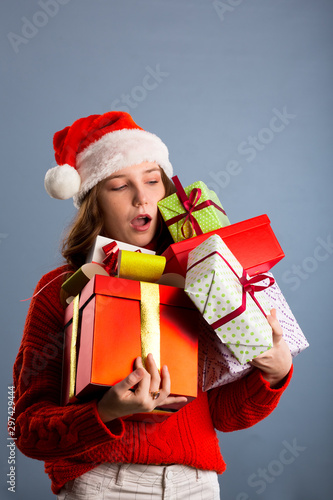 Joyful woman woman holding a lot of boxes with gifts on a gray background.