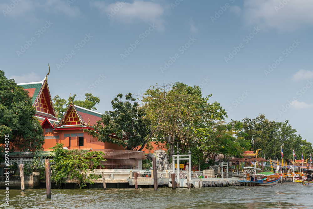 Bangkok city, Thailand - March 17, 2019: Bangkok Noi Canal. Docks with boats at Wat Suwannaram Ratchaworawihan Buddhist temple under blue sky and partly hidden by green trees.