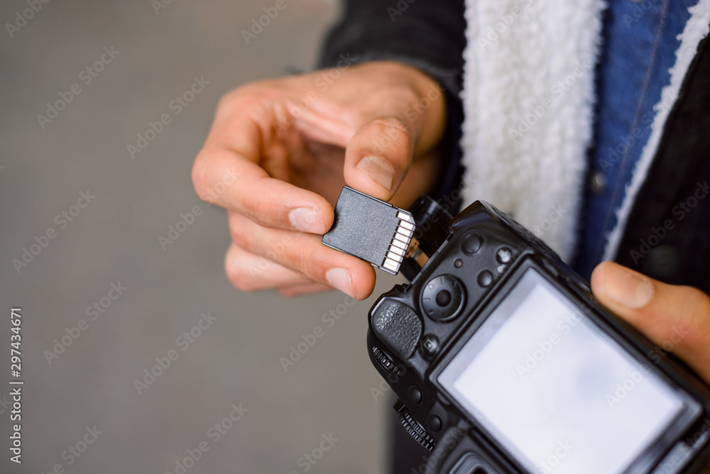 Hand holding SD Card against DSLR camera. Male photographer changing SD card of a photo camera outdoors. Young photographer has run out of storage on his memory stick, changed card on his dslr Hand holding SD Card against DSLR camera. Male photographer changing SD card of a photo camera outdoors. Young photographer has run out of storage on his memory stick, changed card on his dslr