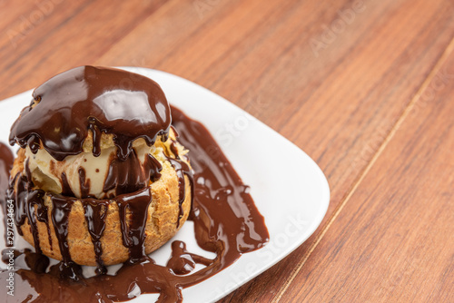 Profiteroles with ice cream and chocolate. Eclairs with black chocolate on wooden background. Traditional French dessert.