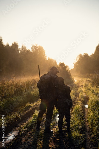 Rifle Hunter and His Son Silhouetted in Beautiful Sunset. Huntsman with a boy and rifle in a forest on a sunrise.