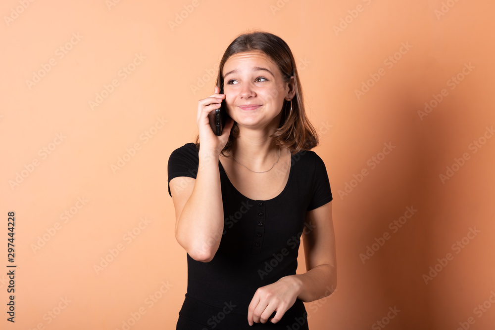 The girl is talking on the phone in surprise, on a light orange background. The girl is talking on the phone in surprise, on a light orange background.