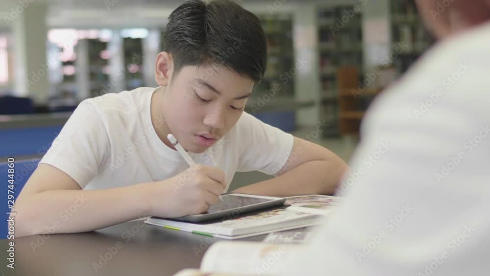 Asian preteens boys using tablet computer at library . Two boy drawing on tablet computer with smile face. Asian preteens boys using tablet computer at library . Two boy drawing on tablet computer with smile face.