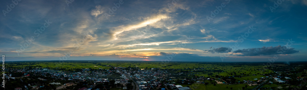 Panorama Top view Aerial photo from flying drone over village in Thailand.Cumulus sunset clouds with sun setting down on dark background.