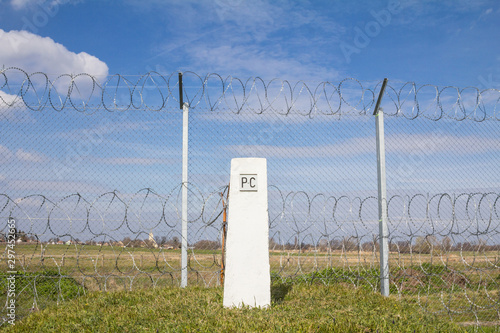 Border fence between Rastina (Serbia) & Bacsszentgyorgy (Hungary) with a boundary marker. This border wall was built in 2015 to stop the incoming refugees & migrants during the refugees crisis photo