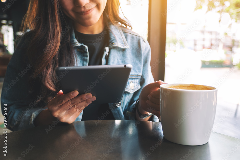 Closeup image of a woman holding and using tablet pc while drinking coffee Closeup image of a woman holding and using tablet pc while drinking coffee