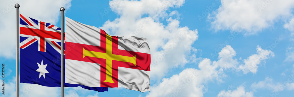 Australia and Guernsey flag waving in the wind against white cloudy blue sky together. Diplomacy concept, international relations. Australia and Guernsey flag waving in the wind against white cloudy blue sky together. Diplomacy concept, international relations.