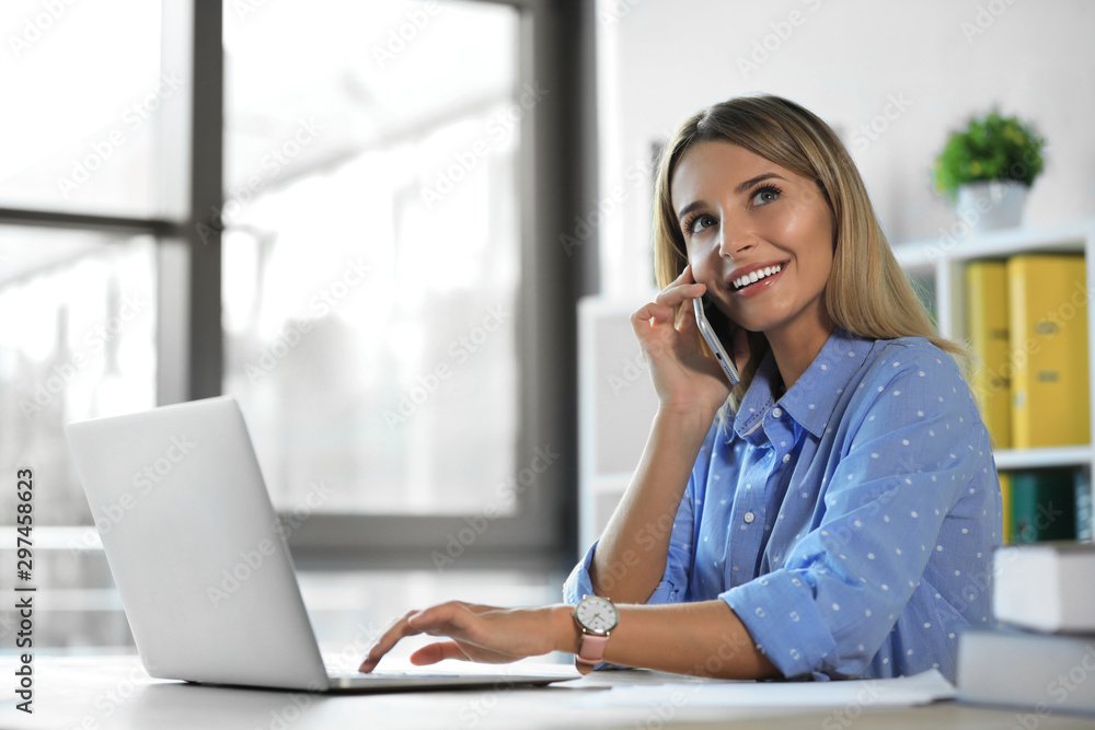 Female business trainer talking on phone while working with laptop in office Female business trainer talking on phone while working with laptop in office