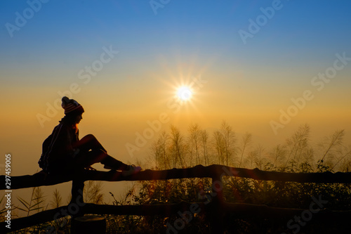 Woman tourist is a feeling relax, she is watching sunrise with mist in the morning, orange sky, viewpoint at Phu Ruea National Park, Loei, Thailand.