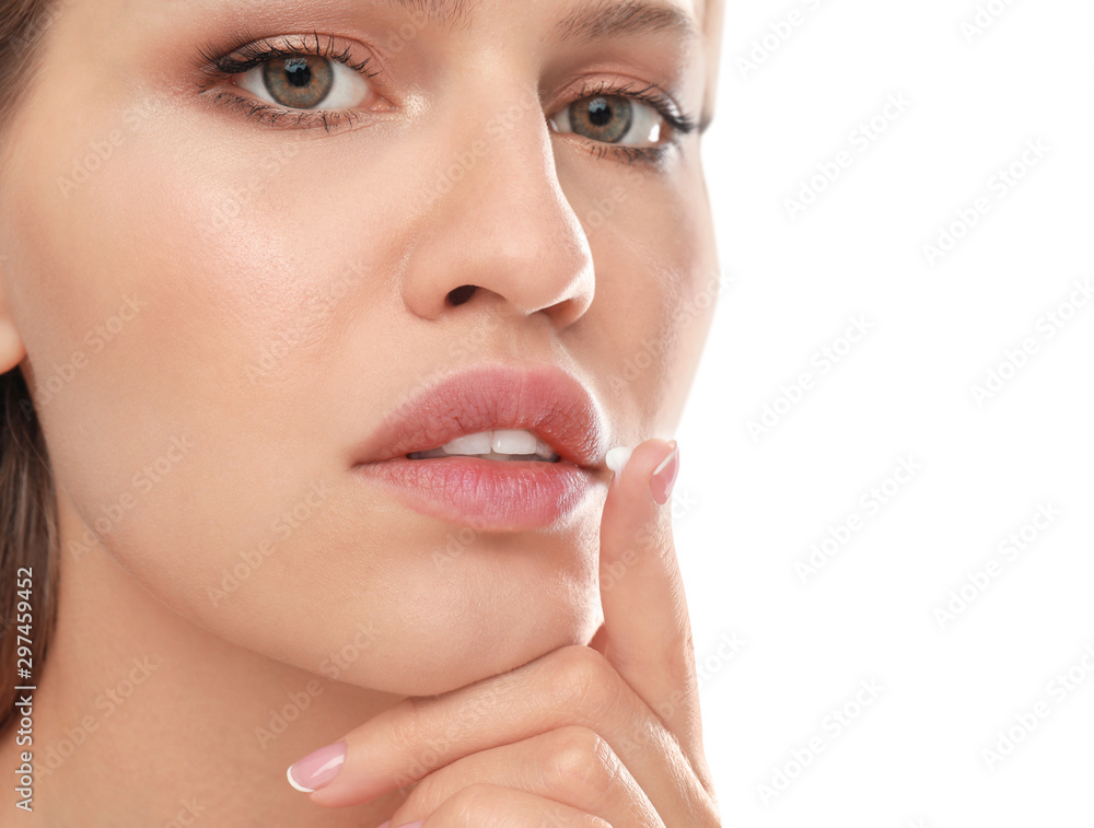 Young woman with cold sore applying cream on lips against white background, closeup