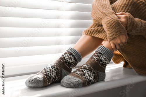 Woman wearing knitted socks on window sill indoors, closeup. Warm clothes