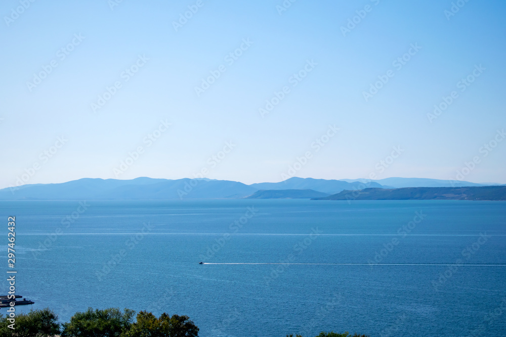 View of a sailing sailboat in calm ocean. Sea and sky background with copy space. View of a sailing sailboat in calm ocean. Sea and sky background with copy space.