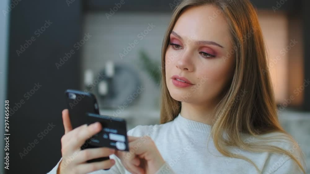 A young beautiful woman holds a smartphone and a credit card while paying for purchases and entering a pincode to pay for delivery. Online shopping A young beautiful woman holds a smartphone and a credit card while paying for purchases and entering a pincode to pay for delivery. Online shopping