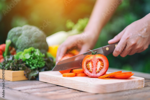 Fotografie Closeup image of a woman cutting and chopping tomato by knife on wooden board
