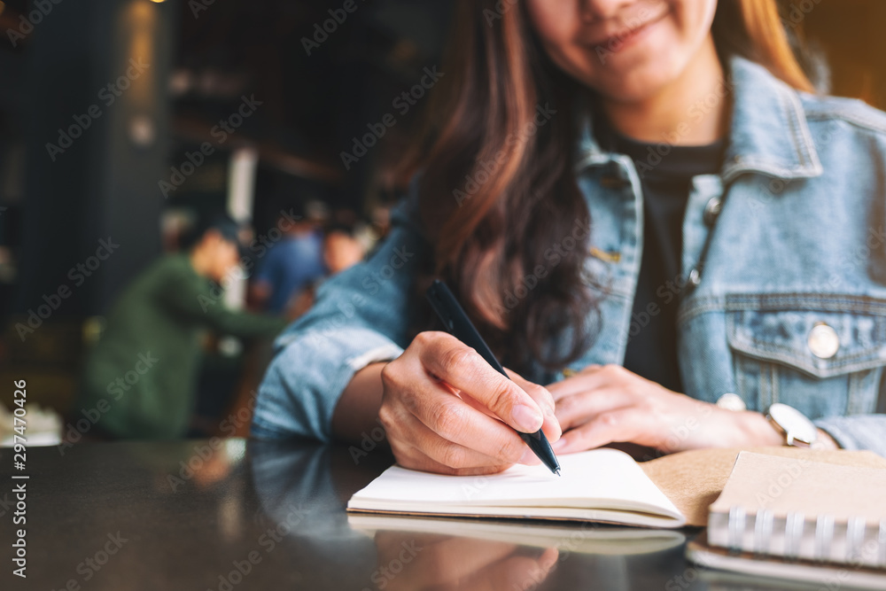 Closeup image of a beautiful asian woman writing on a blank notebook on the table Closeup image of a beautiful asian woman writing on a blank notebook on the table