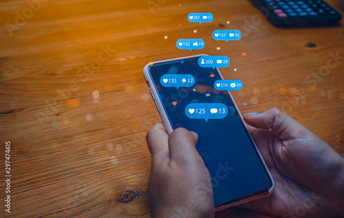Person using a social media marketing concept on mobile phone with notification icons of like, message, comment and star above mobile phone screen.